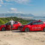 1 moniteur de l'auto-moto école Cristale à la Seyne-sur-Mer devant 2 automobiles rouges sur un parking surplombant la rade de Toulon