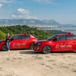 1 monitrice de l'auto-moto école Cristale à la Seyne-sur-Mer devant 2 automobiles rouges sur un parking surplombant la rade de Toulon