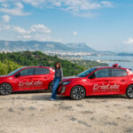 1 monitrice de l'auto-moto école Cristale à la Seyne-sur-Mer devant 2 automobiles rouges sur un parking surplombant la rade de Toulon