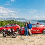 1 moniteur et 1 monitrice de l'auto-moto école Cristale à la Seyne-sur-Mer devant 2 automobiles rouges et une motocyclette sur un parking surplombant la rade de Toulon