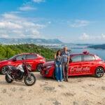 1 moniteur et 1 monitrice de l'auto-moto école Cristale à la Seyne-sur-Mer devant 2 automobiles rouges et une motocyclette sur un parking surplombant la rade de Toulon