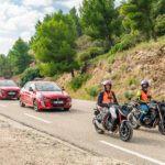 2 motocyclettes et 2 automobiles de l'auto-moto école Cristale à la Seyne-sur-Mer sur une route surplombée par une colline calcaire arborée de pins