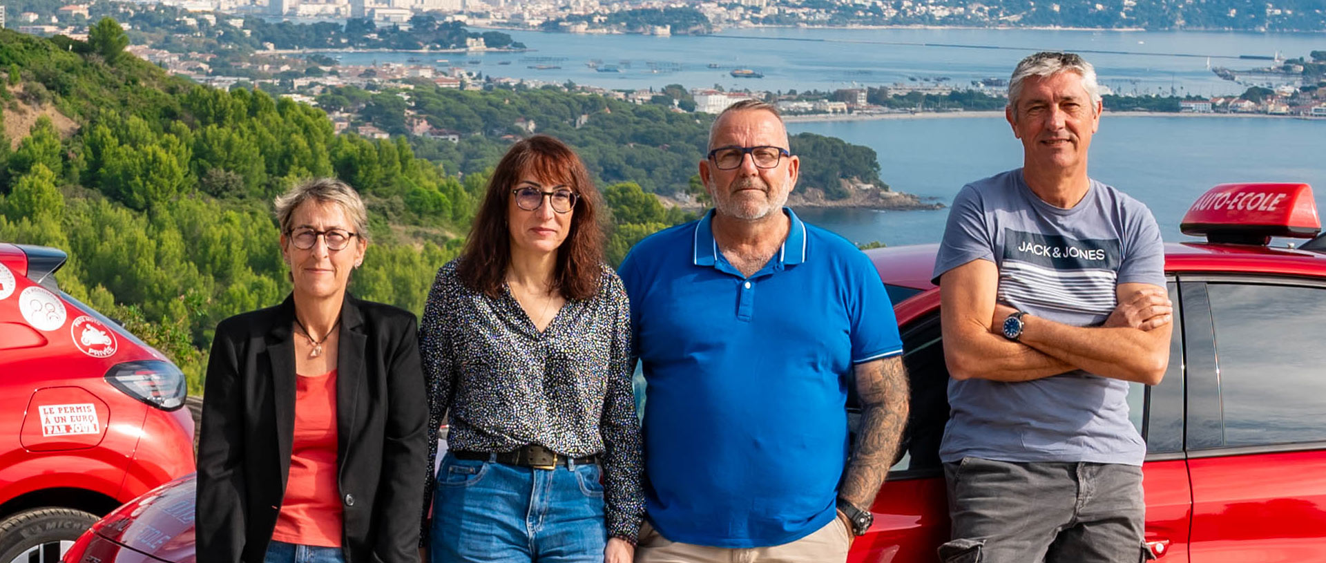 Les 4 moniteurs de l'auto-moto école Cristale à la Seyne-sur-Mer devant 2 automobiles rouges sur un parking surplombant la rade de Toulon